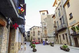Fontanero Borredà trabajando en una calle empedrada del pueblo con casas de piedra y montañas al fondo.