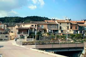 Fontanero Castellolí arreglando tuberías en calle tranquila con casas tradicionales y montañas al fondo