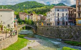 Fontanero La Pobla de Lillet, calle empedrada con casas de piedra y montañas verdes al fondo