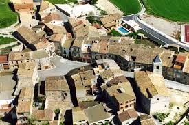 Fontanero Montmaneu, calle tranquila con casas tradicionales y un fontanero trabajando en una tubería exterior.