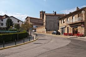 Fontanero Olvan reparando tubería en calle empedrada del centro urbano con casas de piedra y montaña al fondo