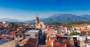 Fontanero Sant Celoni, calle típica con fachadas coloridas y montañas al fondo en un día soleado.