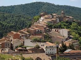 Fontanero Santa Maria d'Oló calle con casas de piedra y montañas al fondo, ambiente rural y tranquilo
